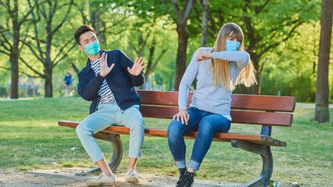 Mann und Frau mit Mundschutzmaske auf einer Parkbank in einem Stadtpark. (Symbolbild)