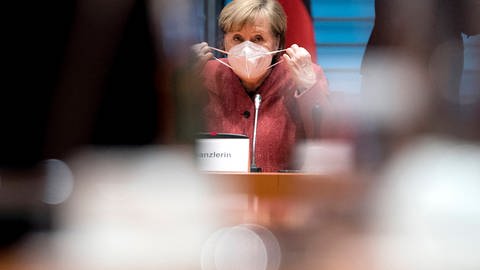 Angela Merkel nimmt ihre Maske ab.