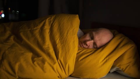 Ein Mann schläft eingewickelt in seine Bettdecke.