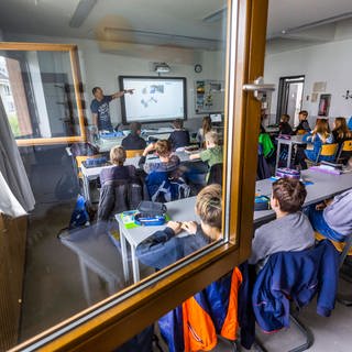 Schüler*innen sitzen in einem Klassenzimmer bei geöffnetem Fenster