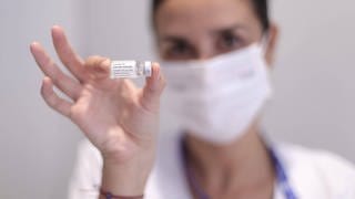 Frau mit Maske hält J&J-Impfdose in Kamera