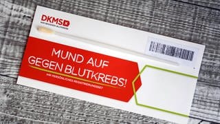 DKMS-Logo auf einem Umschlag mit dem Test-Stäbchen für die Typisierung potentieller Spender mit Zellen der Mundschleimhaut. 