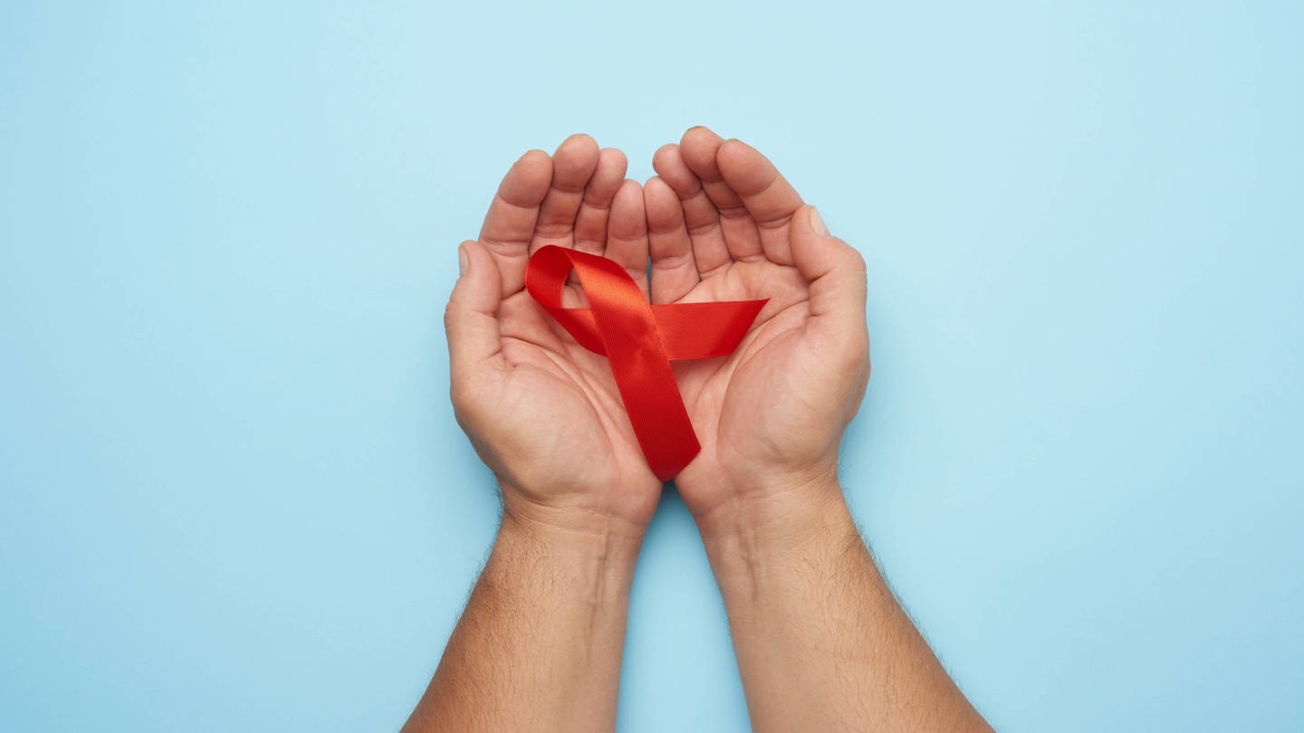 Hände eines Mannes halten eine rote Schleife - ein Symbol für den Kampf gegen AIDS.