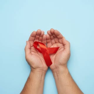 Hände eines Mannes halten eine rote Schleife - ein Symbol für den Kampf gegen AIDS.