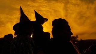 Das Bild zeigt die Silhouette von drei Personen mit Hexenhut auf.