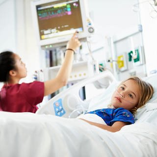 Das Bild zeigt ein Mädchen, das in einem Krankenhaus behandelt wird und an ein Sauerstoffgerät angeschlossen ist.