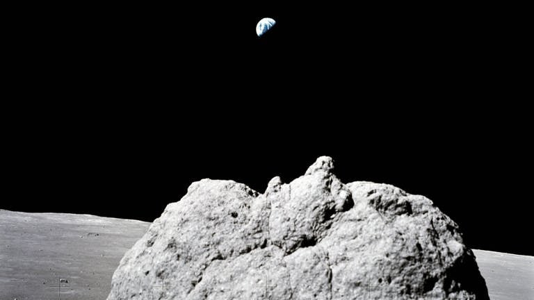 Der weit entfernte Hintergrund der Erde ist über einem großen Mondfelsenvordergrund auf dem Mond zu sehen. Das Foto wurde mit einer Hasselblad-Handkamera von den letzten beiden Mondwanderern des Apollo-Programms aufgenommen.