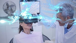 Eine Frau auf einer Behandlungsliege trägt eine VR-Brille und lacht, während ein Mann den Sitz der VR-Brille bei ihr überprüft.