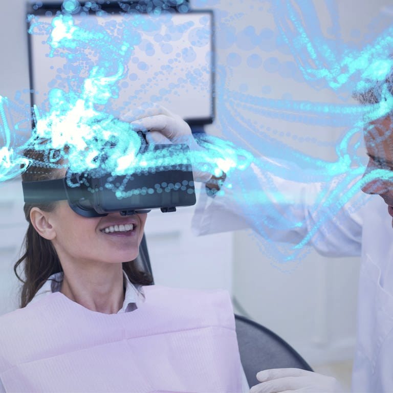 Eine Frau auf einer Behandlungsliege trägt eine VR-Brille und lacht, während ein Mann den Sitz der VR-Brille bei ihr überprüft.