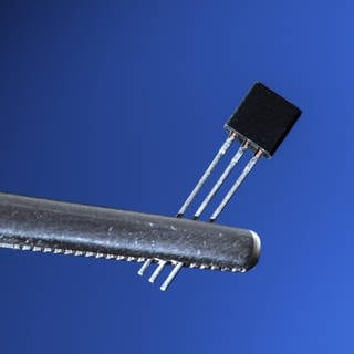Ein elektronischer Transistor wird von einer Pinzette gehalten.
