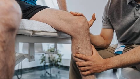 Physiotherapeut berührt das Knie eines männlichen Patienten.