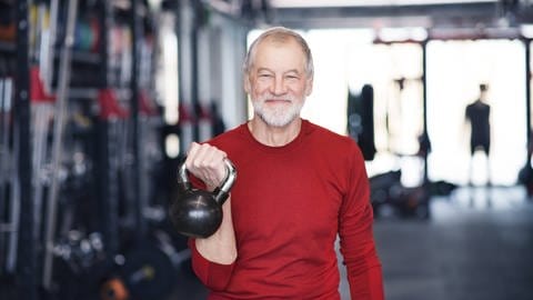 Älterer Mann beim Training mit der Kettlebell im Fitnessstudio.