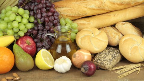 Verschiedenes Obst, Zwiebeln, Knoblauch, Saft und Brot liegen auf einem Tisch präsentiert.