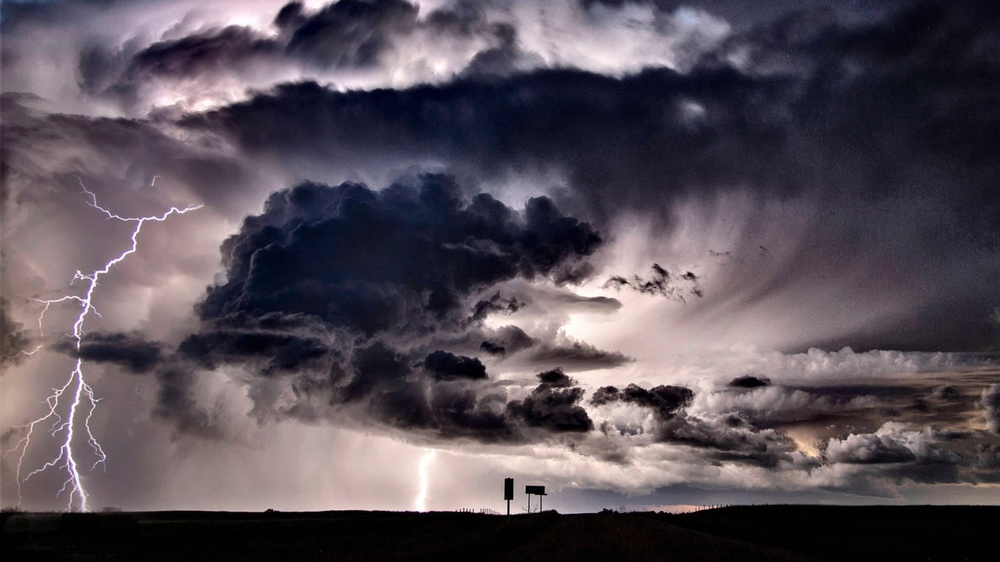 Ein Blitz schlägt aus einer dunklen Gewitterwolke auf die Erdoberfläche ein.