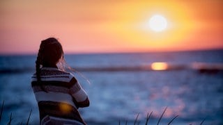 Eine Frau beobachtet den Sonnenaufgang über dem Meer.