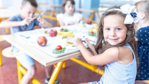 Kind sitzt beim Essen in der Schule. Sie hat ein Essen mit Obst und Gemüse vor sich.