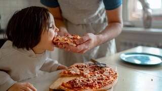 Kind wird von dem Vater mit einer Pizza gefüttert.