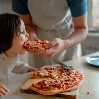 Kind wird von dem Vater mit einer Pizza gefüttert.