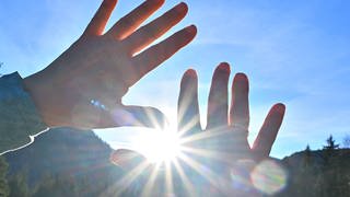 Hände werden versucht schützend vor Sonnenstrahlen zu halten, aber die Sonnenstrahlen kommen zwischen den Fingern durch.