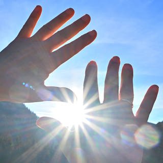 Hände werden versucht schützend vor Sonnenstrahlen zu halten, aber die Sonnenstrahlen kommen zwischen den Fingern durch.