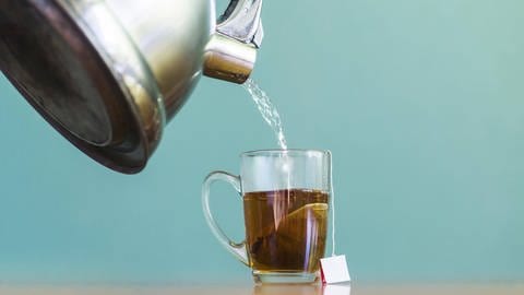 Tee wird aus einem Teekessel in eine Glastasse eingegossen.