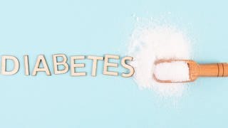 Auf einem Tisch ist das Wort "Diabetes" mit Holzbuchstaben ausgelegt. Daneben ist Zucker gestreut.