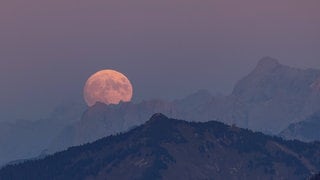 Rötlicher Mond geht über Berge auf.