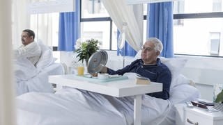 Das Bild zeigt einen älteren Herrn im Krankenhaus mit Krankenhausessen. Symbolbild.
