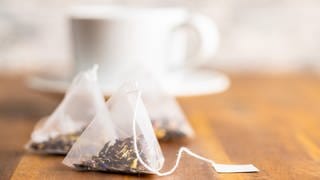 Teebeutel liegen vor einer Teetasse: Seit Jahren wird Tee verstärkt in pyramidenförmigen Kunststoffbeuteln angeboten. Teebeutel wie früher aus einfacher Zellulose, also Papierfasern, werden weniger. 