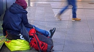 Eine obdachlose Person sitzt auf der Straße mit ihren Habseligkeiten.
