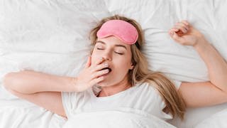 Viele Menschen sehnen sich nachts nach besserem Schlaf. Welche Tipps geben Studien? Das Bild zeigt eine Frau, die im Bett liegt und gähnt. Symbolbild.