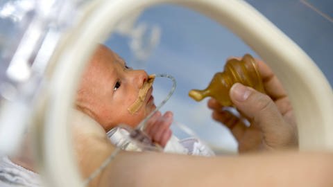 Ein Frühgeborenes bekommt tropfenweise Muttermilch durch einen Sauger angeboten. So soll der natürliche Saugreflex des Kindes geweckt werden.