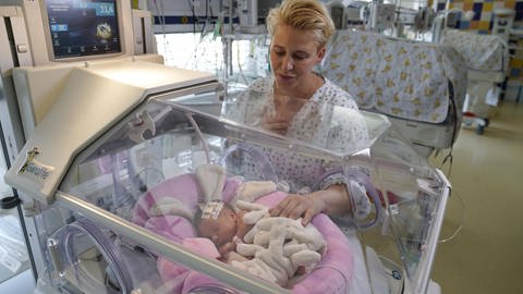 Mutter bei ihrem Neugeborenen in einem Inkubator