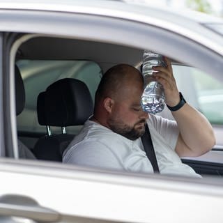Mann sitzt im Auto und hält sich zur Abkühlung eine Wasserflasche an den Kopf.
