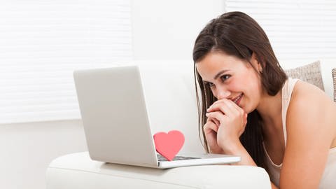 Das Bild zeigt eine Frau, die grinsend auf ihren Laptop schaut.