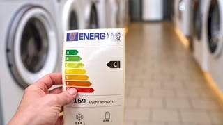 Energieeffizienz-Label vor einem Gang von Waschmaschinen. 