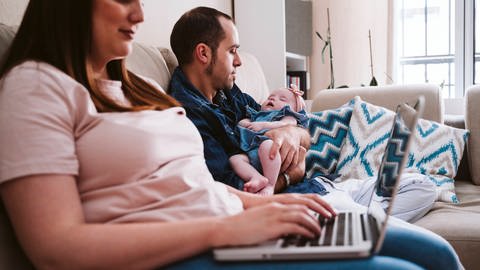 Frau arbeitet am Rechner, Mann hält schlafendes Kind