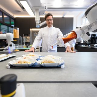 Koch Benjamin Biedlingmaier steht in der Roboterküche der TU Dresden und beobachtet einen Roboter beim Zubereiten eines Salats. Menschen sollen künftig in der Lage sein, in Echtzeit mit Robotern oder Maschinen zu interagieren. An der TU Dresden wird dazu geforscht.