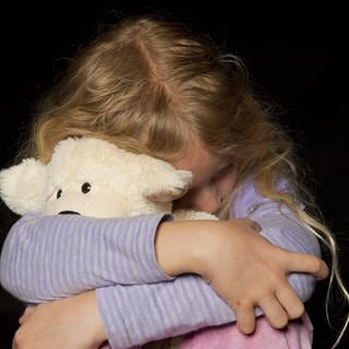 Mädchen kauert und hat einen Teddybären im Arm