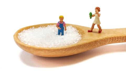 Zwei Kinderspielzeugfiguren stehen auf einem Holzlöffel voller Zucker.
