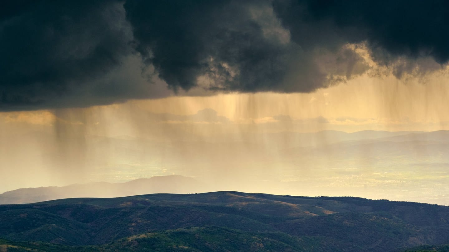 Neuen Forschungsergebnissen zufolge gab es wohl schon vor 4 Milliarden Jahren den Wasserkreislauf und damit Regen auf der Erde | Dunkle Wolken und Regen über einer Hügellandschaft