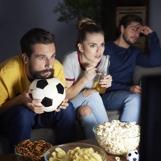 Besorgte Freunde sitzen auf dem Sofa und schauen Fußball.
