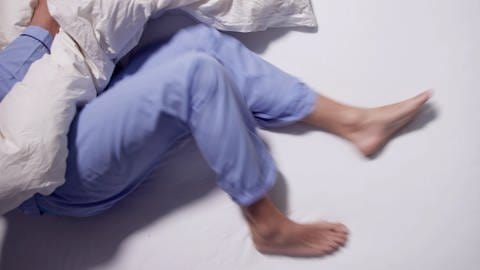 Person mit Restless-Legs-Syndrom liegt in Bett. Die Beine bewegen sich.