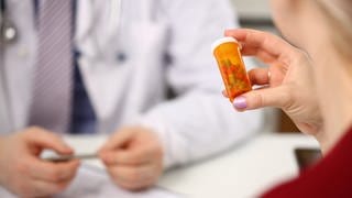 Frau beim Arzt hält ein Döschen mit Pillen, tags: Wechseljahre, biidentische, Hormone, Therapie
