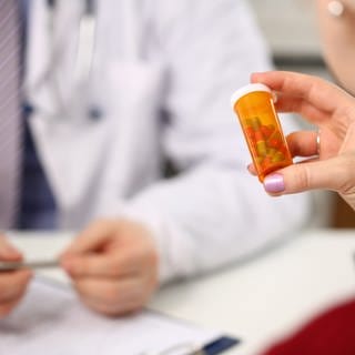 Frau beim Arzt hält ein Döschen mit Pillen, tags: Wechseljahre, biidentische, Hormone, Therapie