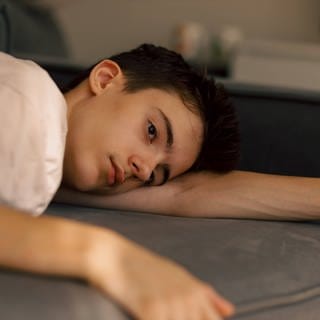 Jugendliche und junge Erwachsene sind einer neuen Studie zufolge immer unglücklicher | ein trauriger Junge liegt auf der Couch