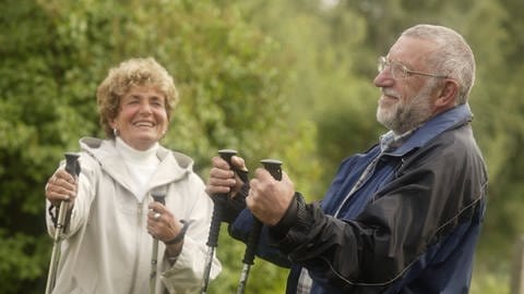 Älteres Paar mit Nordic-Walking-Stöcken: Durch Rollatoren verlernen die Nutzer:innen selbst ihr Gleichgewicht gut zu halten. Nordic-Walking-Stöcke können eine gute Alternative zu Rollatoren sein. Sie können Sicherheit geben und die Fitness fördern.