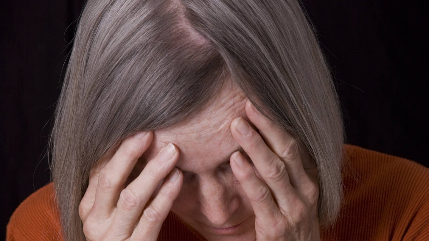 Gestelltes Bild zum Thema Demenz - Eine ältere Frau greift sich an den Kopf.