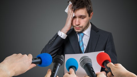 Nicht nur Schimpansen geraten durch Zuschauer unter Druck, sondern auch Menschen. Dieser Mann wird sichtlich nervös, als er vor einem Publikum mit Mikrofonen sprechen soll.