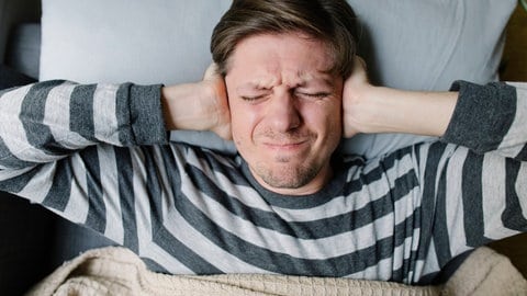 Symbolbild: Mensch, der sich im Bett die Ohren zuhält. Die Rakete Starship könnte in Zukunft Menschen aus dem Schlaf reißen.